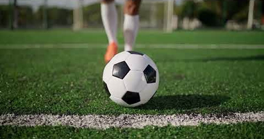 Bola de futebol sobre a linha do campo com um jogador ao fundo desfocado