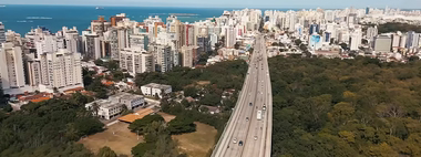 Vista aérea de área urbana brasileira com avenida, prédios e áreas verdes em cena da websérie Feito no Brasil