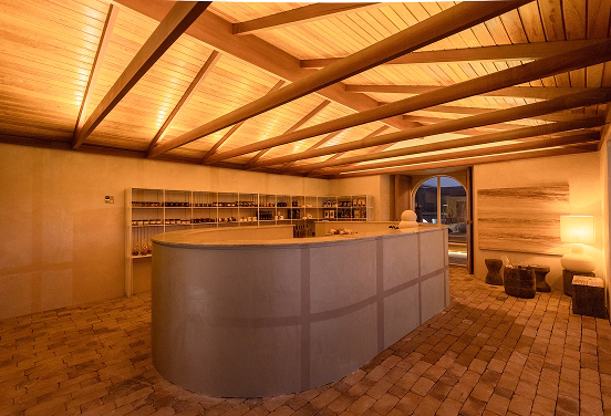 Ambiente interno da CASACOR Minas 2026 com balcão central, estrutura de madeira no teto e iluminação aconchegante